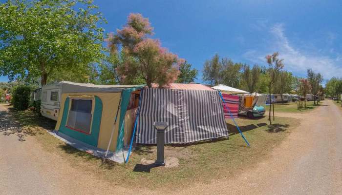 Une caravane et son auvent sur un emplacement, sous les tamaris